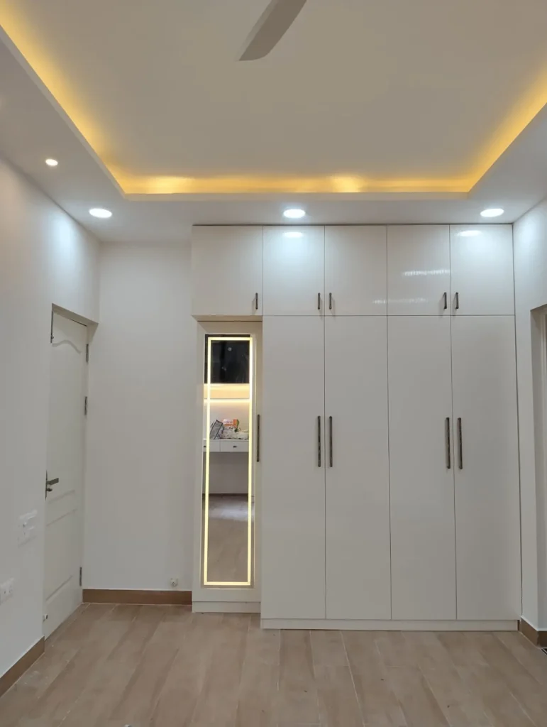 Floor-to-ceiling white wardrobe with loft, lit full-length mirror and cove-lit ceiling, House Decors, Chennai