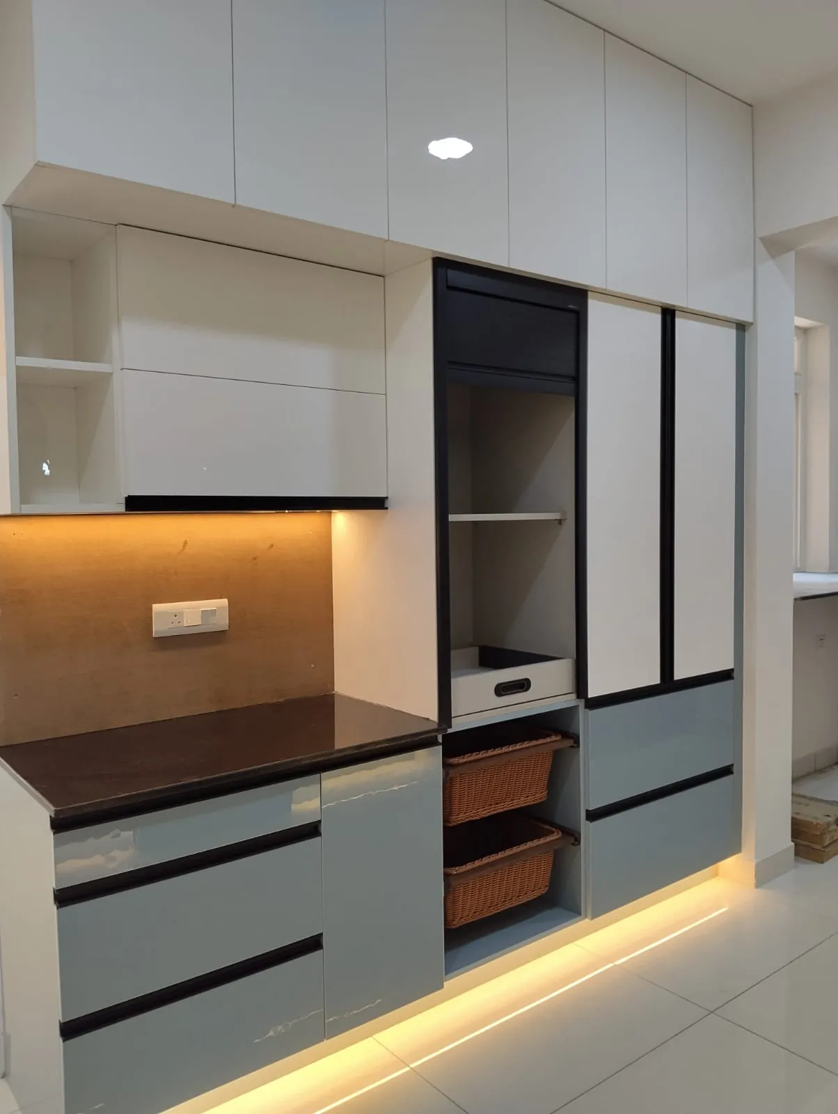 Kitchen tall unit with a pull-out tray, roller shutter, wicker baskets and LED lights under the cabinets and along the base, House Decors, Chennai