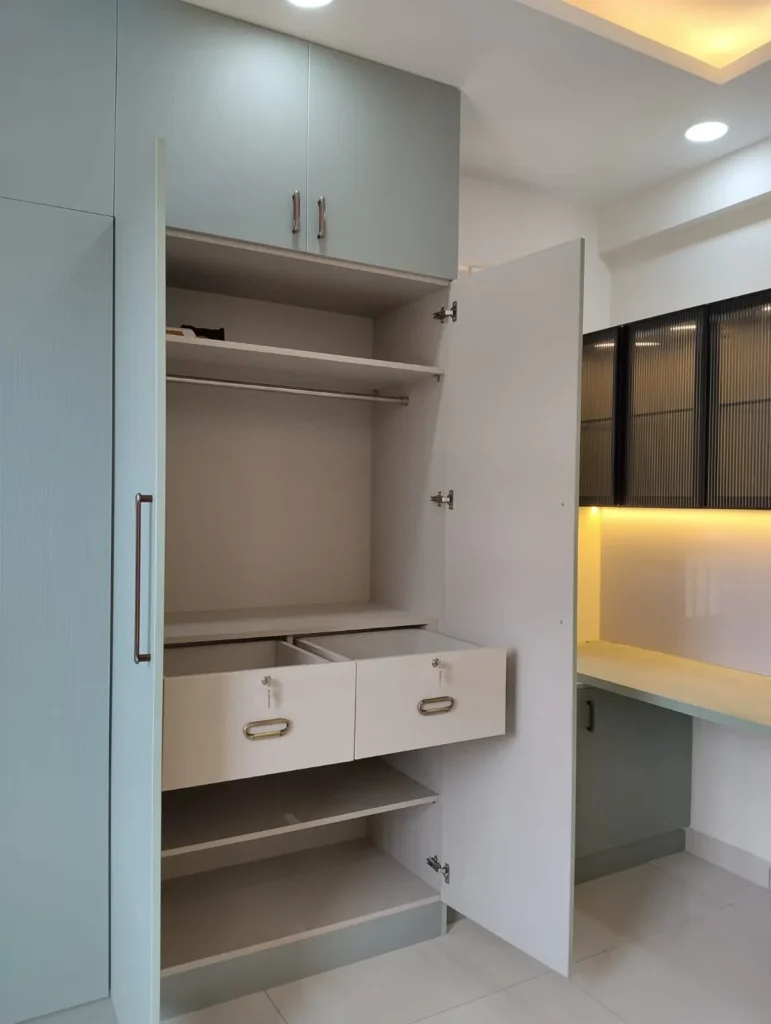 Open sage-green wardrobe showing hanging rail, shelves and two drawers with locks, with a study desk beside it, House Decors, Chennai